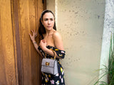 Gaia Handbag Grigio held by a female model with dark brown hair wearing a headband, black floral dress and leaning against an old door. 